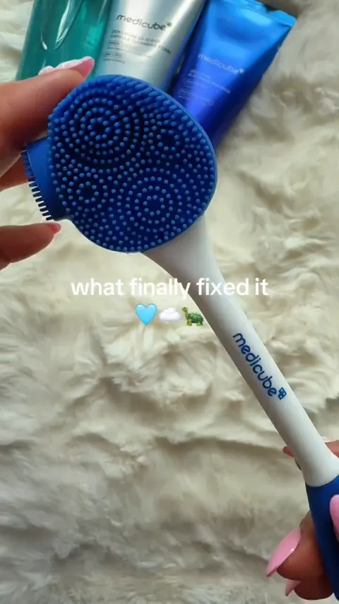 A hand holding a silicone face brush beside the products