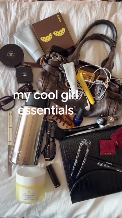 A bag spilled out on a bed with the text my cool girl essentials